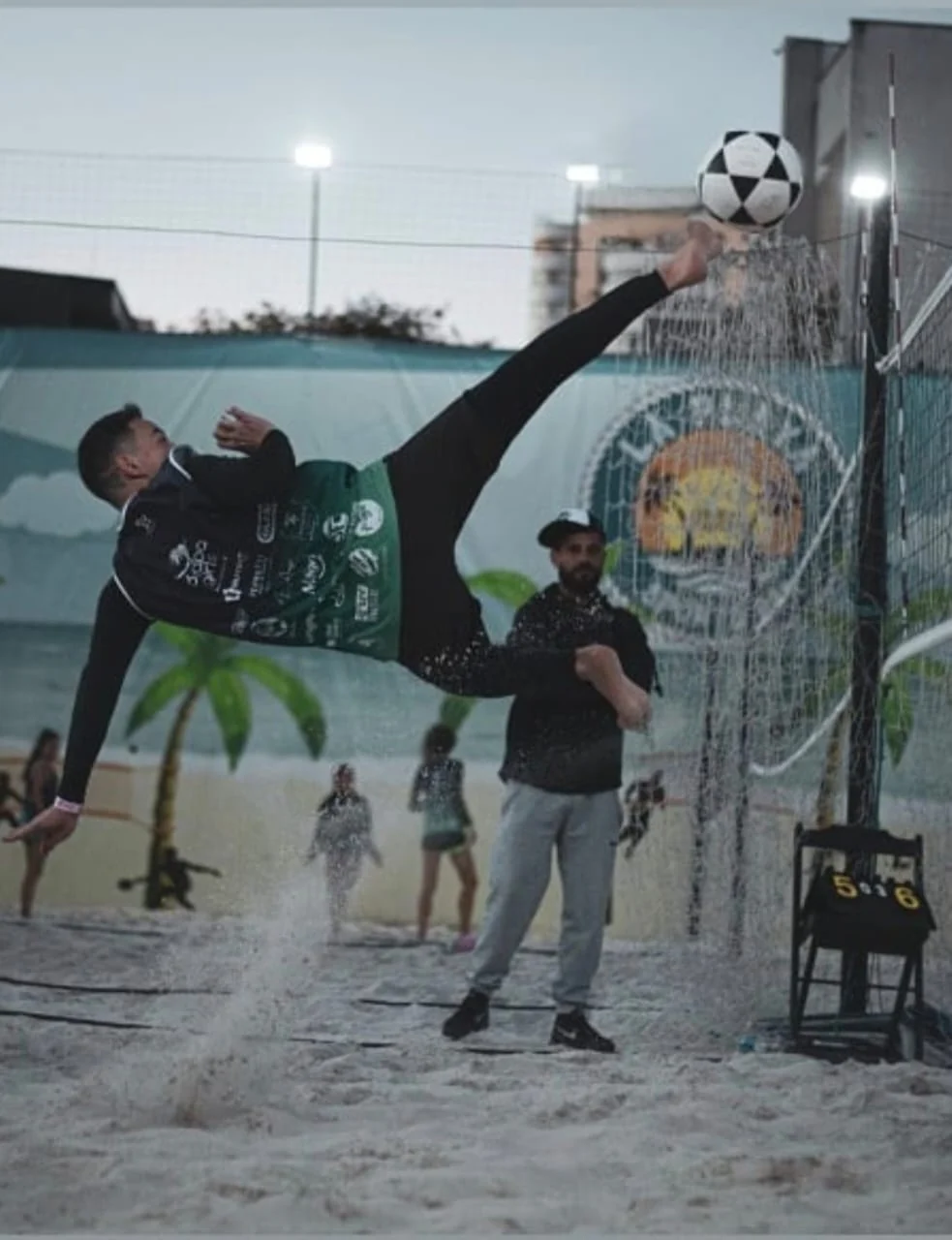 Atleta executando bicicleta acrobática em partida de futevôlei