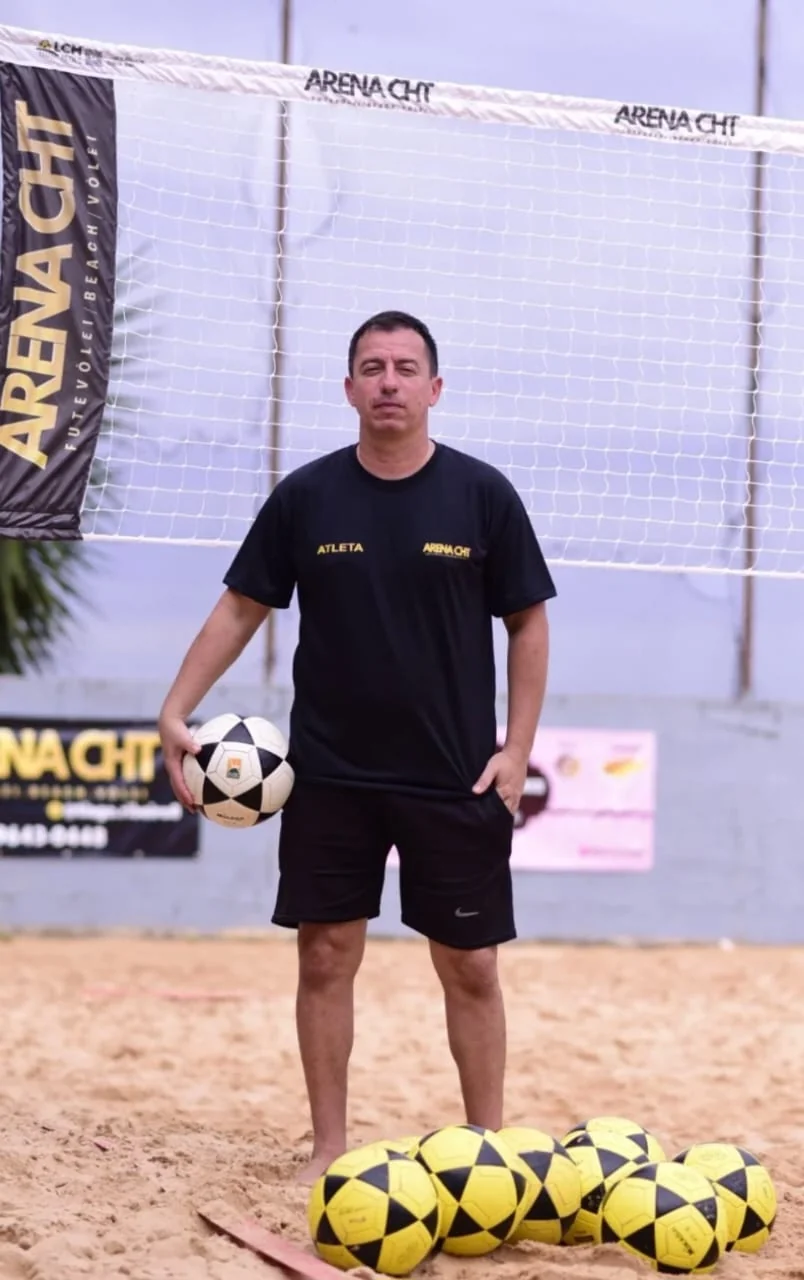 Professor Tiago Ribeiro, fundador da Arena CHT, na quadra de areia com bolas de futevôlei